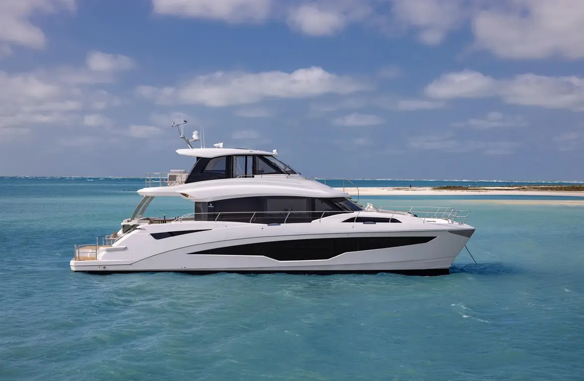 Luxury yacht cruising in clear blue waters with a sandy beach and clouds in the sky, showcasing modern design and elegance.